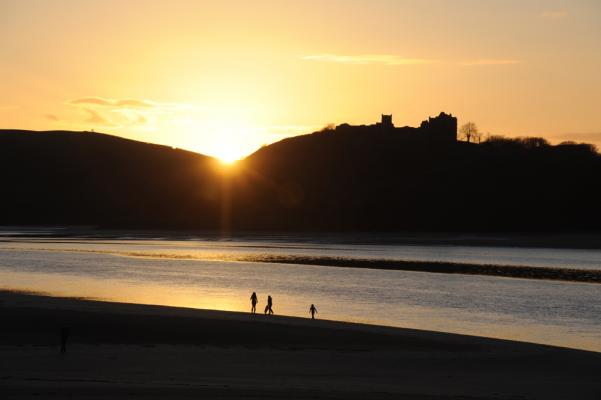 A family plays on the beach at low tide as the sun falls behind Llansteffan Castle March 2011